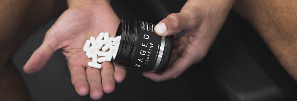 Close-up of Kaged PurCaf caffeine capsule jar showcasing white capsules poured into a hand with a dark gym bench background