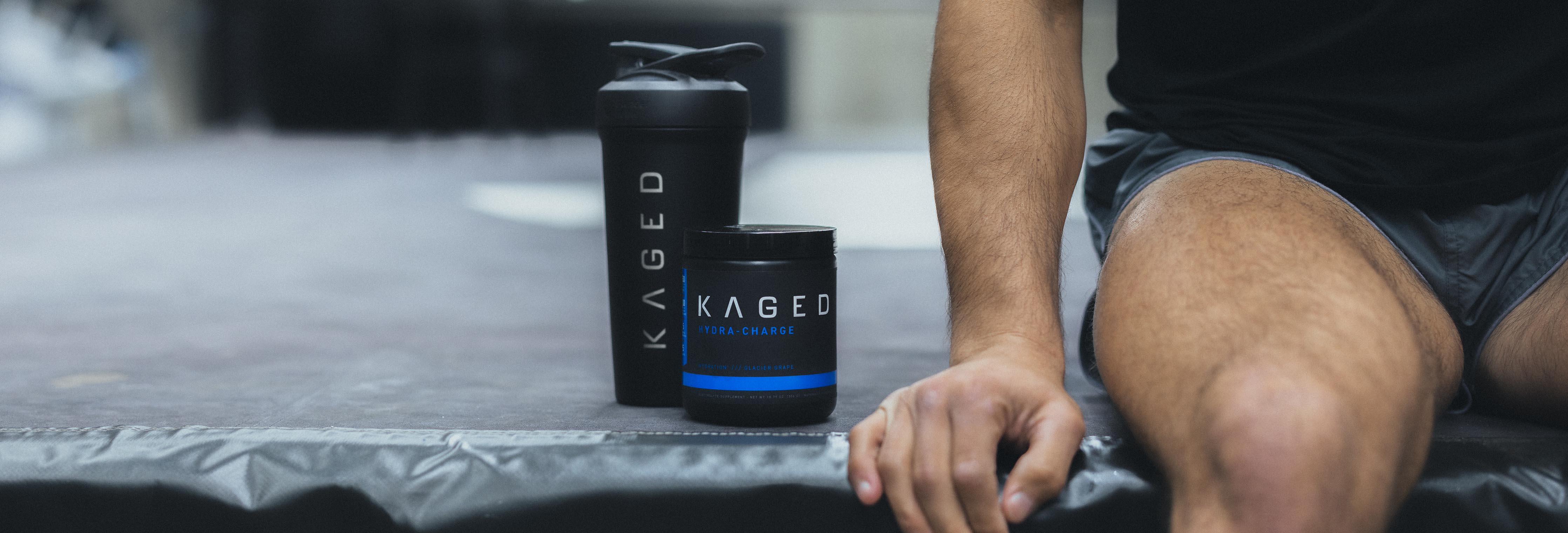 Man seated resting beside a KAGED shaker bottle and supplement tub on a gym mat