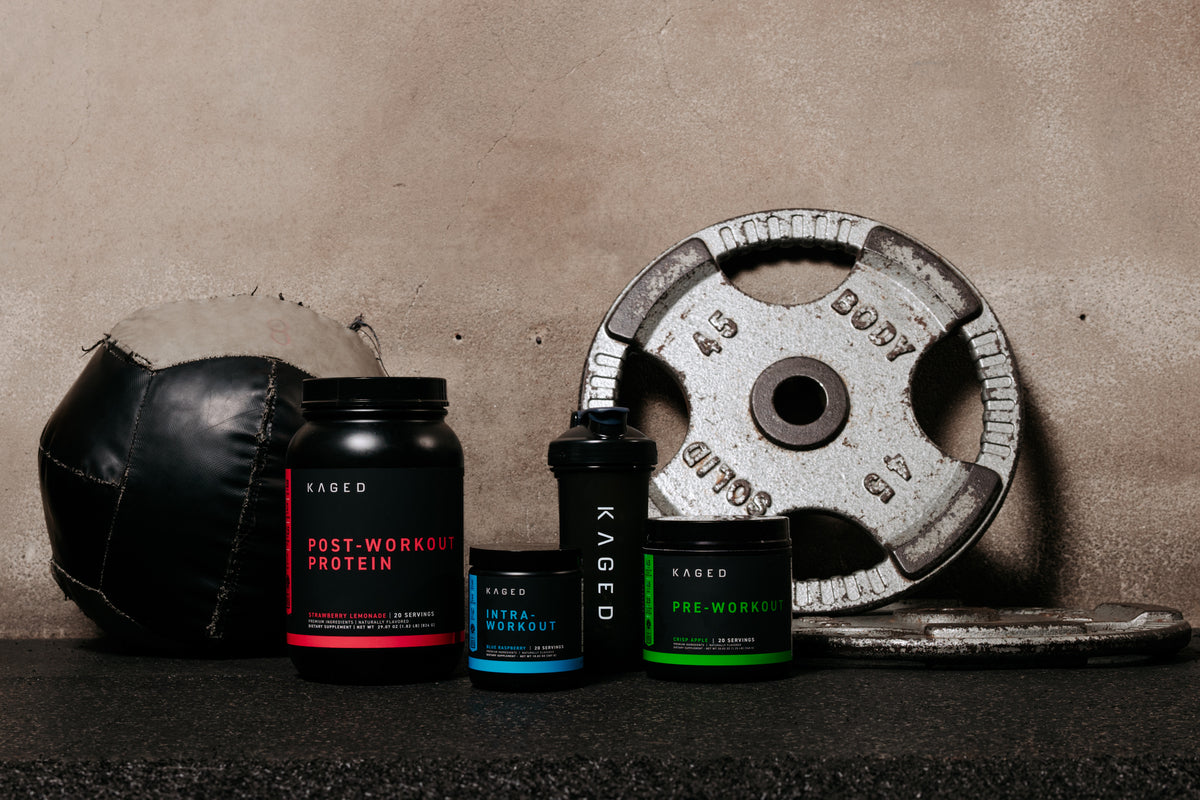 Front view of KAGED Post-Workout, Intra-Workout, and Pre-Workout tubs with a KAGED shaker, medicine ball, and 45 lb plate