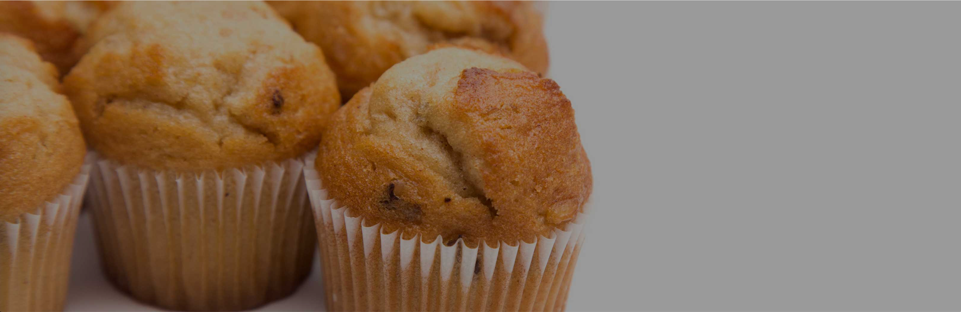 Close-up of vanilla protein cupcakes made with Clean Meal, golden-brown tops and paper liners on a light gray background