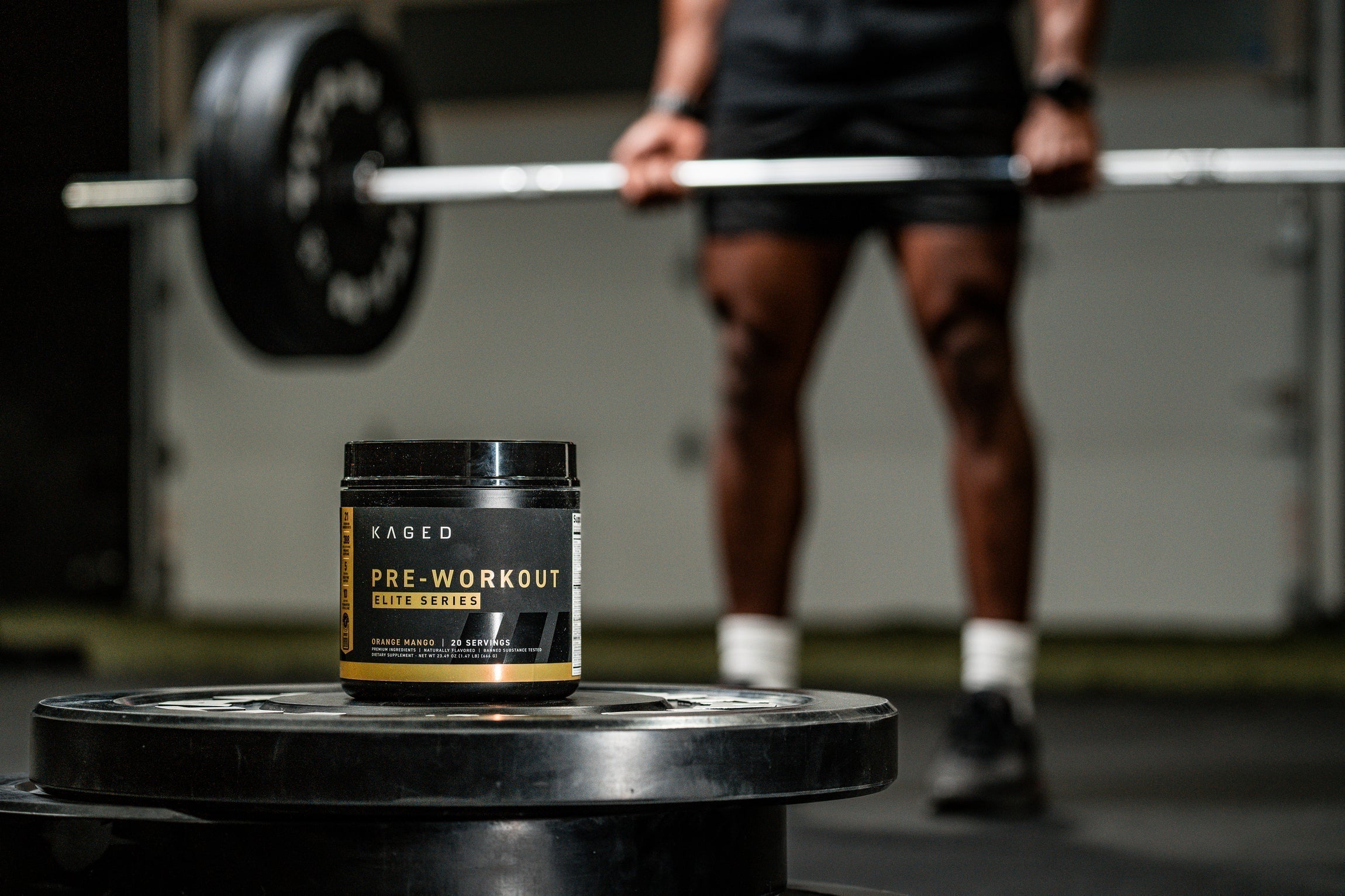 Front view of KAGED Pre-Workout Elite Series tub showing the pre-workout label and flavor with an athlete deadlifting in a gym