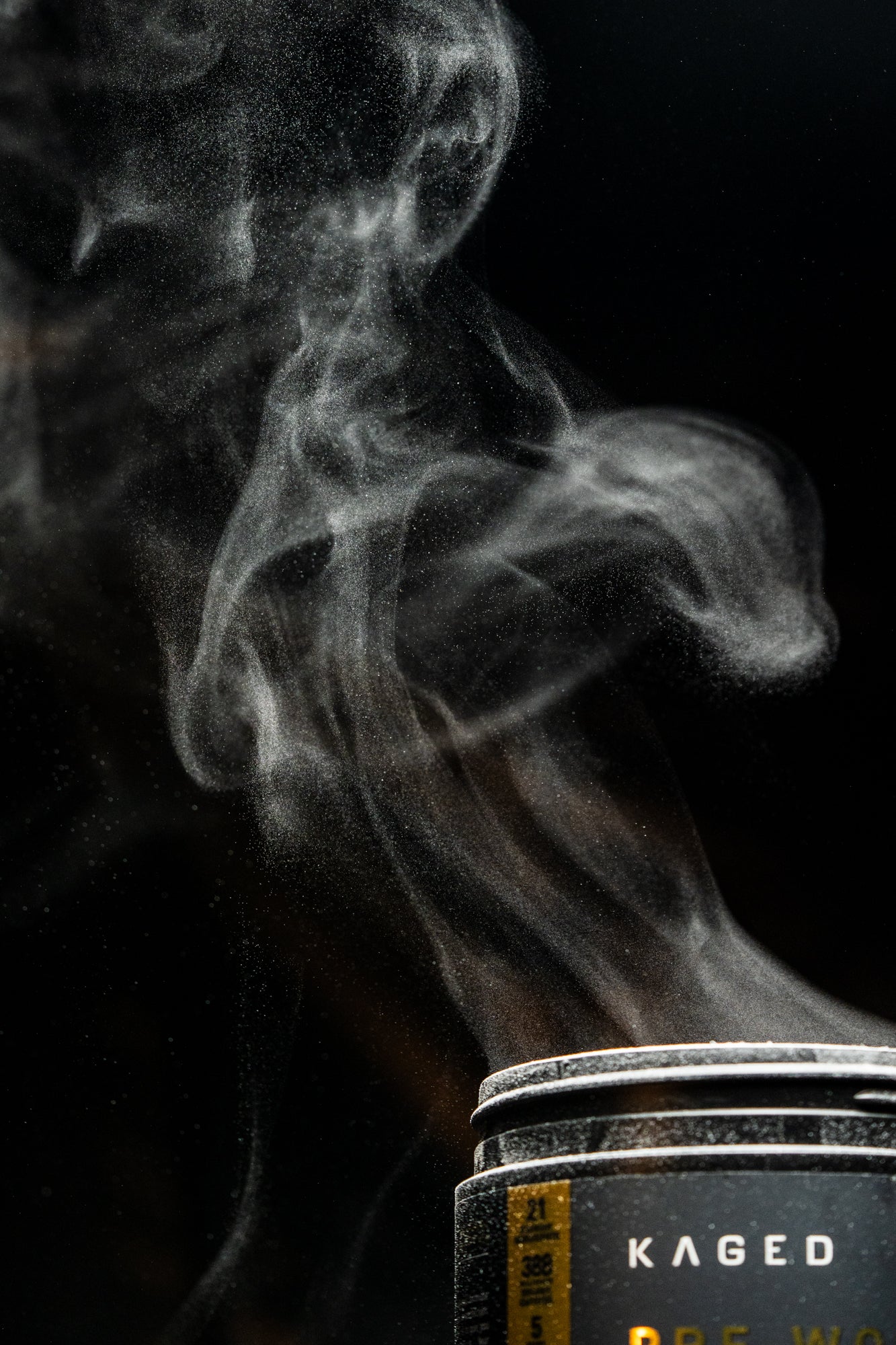 Close-up of Pre-Workout Elite tub with powder plume and KAGED logo against black background