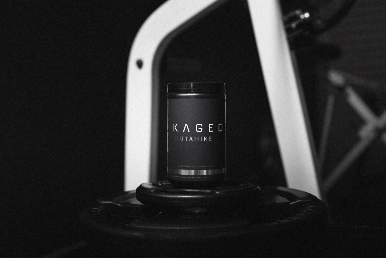 Kaged Glutamine container sitting on weight plates in a dark gym setting