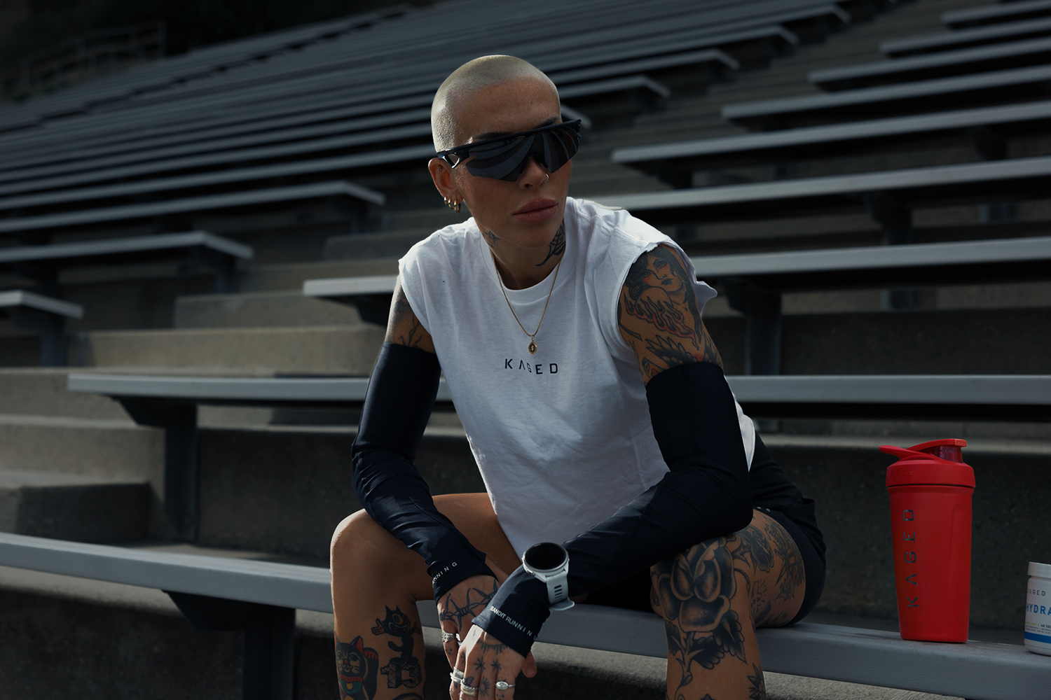 Athlete sitting on stadium bleachers resting, red KAGED Strada shaker bottle on the bench beside them
