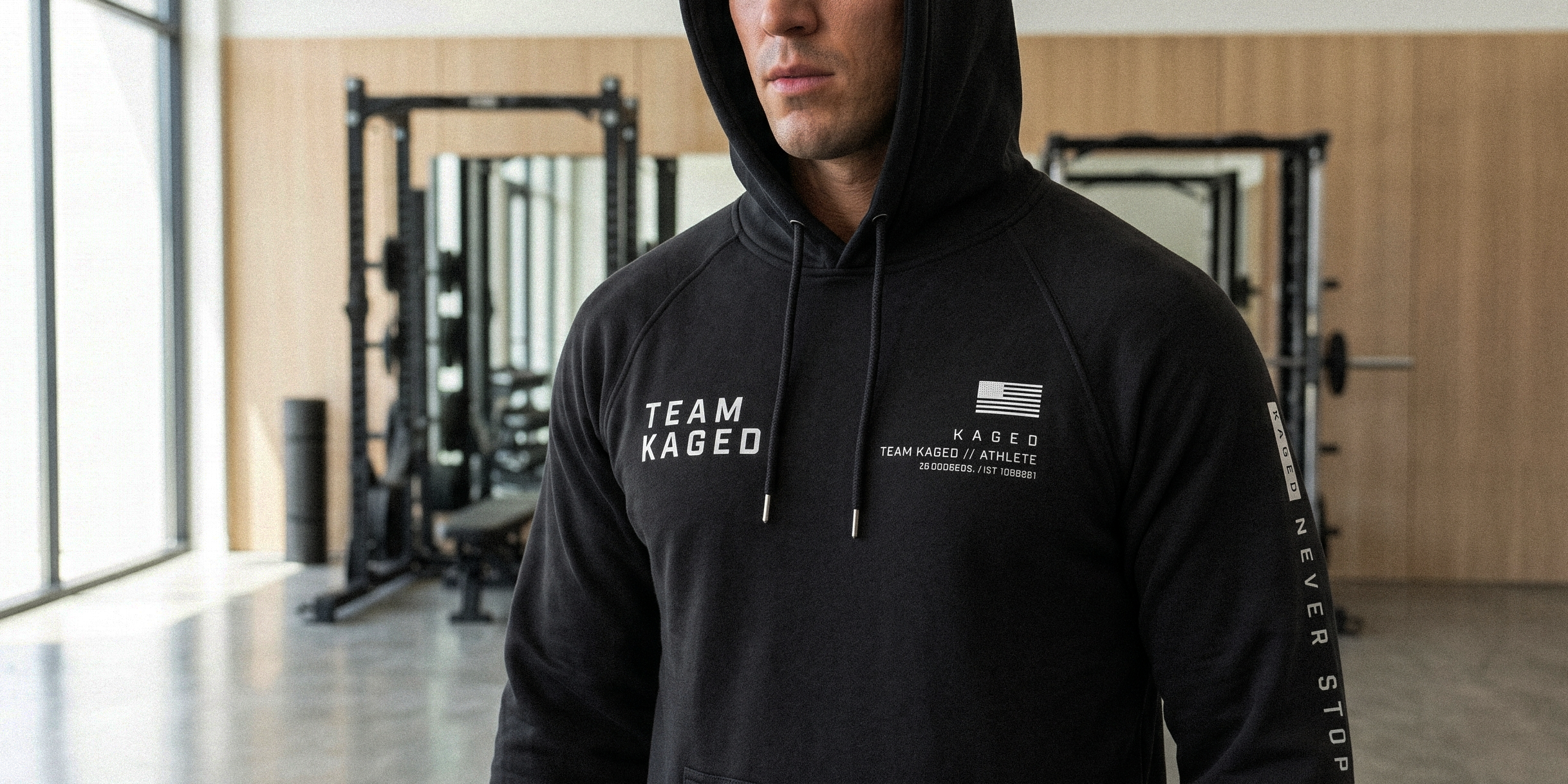 Front view of Team Kaged black heavyweight hoodie showing ‘TEAM KAGED’ chest text and flag logo, raglan sleeves in gym